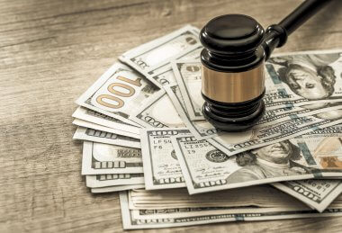 A gavel head resting on a stack of United States hundred dollar bills.